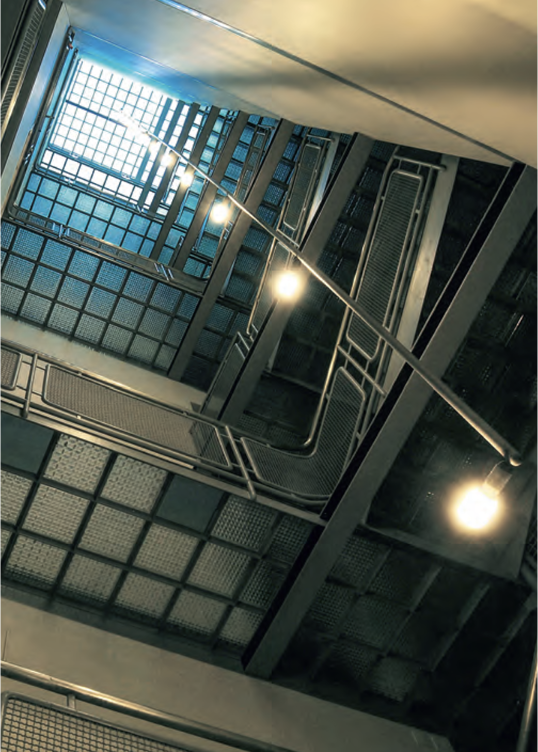 Blick nach oben in ein industrielles Treppenhaus mit Gitterstufen, Geländern, Lichtquellen und einem Oberlicht, Corbusier